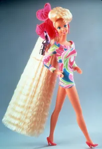 A studio product shot of Totally Hair Barbie in her iconic 90s geometric-print minidress, showing off ultra-long floor-length crimped blonde hair tied back with oversized pink scrunchies.