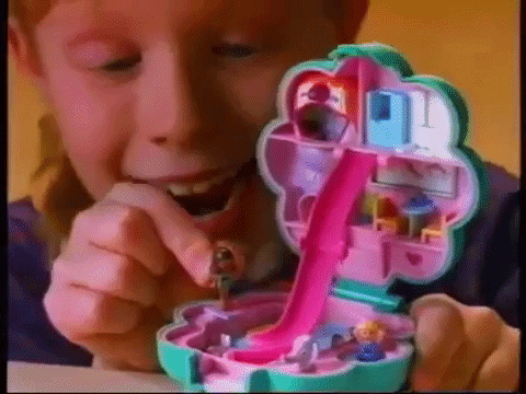 An animated GIF from a 90s Polly Pocket TV commercial showing a young girl placing a micro figure onto the slide of a pastel-pink treehouse compact.