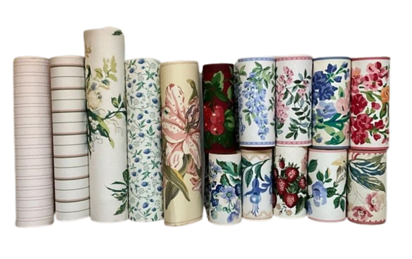 A collection of rolled vintage wallpaper border strips lined up, displaying floral, berry, and striped patterns.