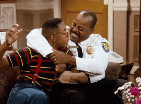 Animated GIF from Family Matters showing police officer Carl Winslow (Reginald VelJohnson) smiling as he holds Steve Urkel (Jaleel White) in a friendly headlock in the Winslow living room.