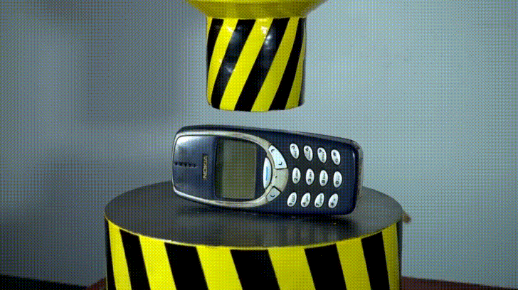 Hydraulic Press Channel showing a heavy industrial press lowering down toward an indestructible dark blue Nokia 3310 phone.