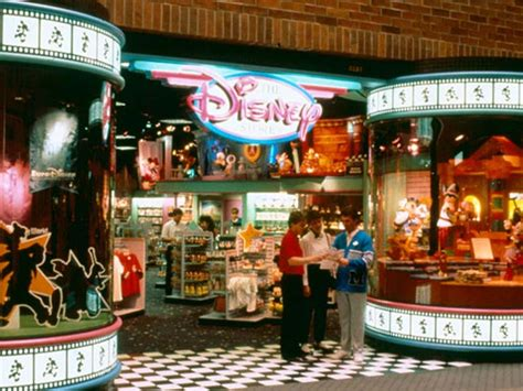 An interior mall photo of a 1990s Disney Store entrance, framed by film-strip archways, checkered tile floors, and plush character displays.