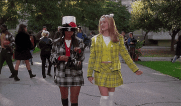 An animated GIF from Clueless showing Dionne Davenport (Stacey Dash) and Cher Horowitz (Alicia Silverstone) strutting down a Beverly Hills high school walkway in their iconic plaid blazer-and-skirt suits.