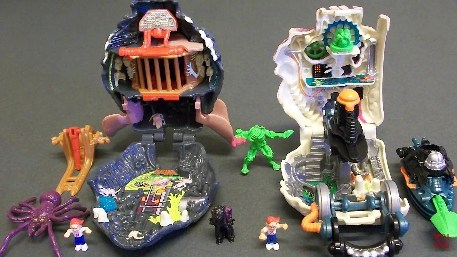 A static photo of opened Mighty Max micro playsets arranged on a table with their miniature hero figures, alien pods, and monster accessories.
