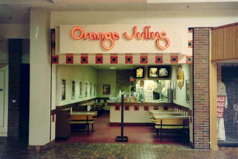 An original retro Orange Julius mall location featuring bright red neon script signage, tiled counter accents, and menu boards promising frothy blended citrus treats.