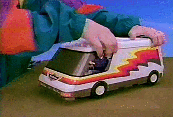An animated GIF from a 90s Micro Machines commercial showing a kid driving a white camper van with rainbow stripes across a table before unfolding it.