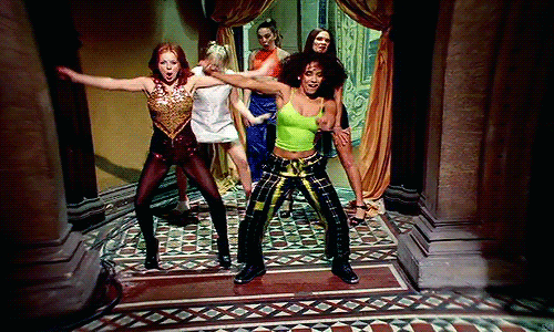 An animated GIF from the Spice Girls' "Wannabe" music video, featuring Scary, Sporty, Baby, Ginger, and Posh dancing wildly down a grand hotel hallway.