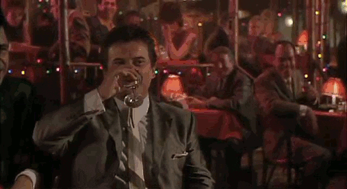 An animated GIF from Goodfellas showing Tommy DeVito (Joe Pesci) taking a sip of his drink and bursting into a booming laugh at a dim nightclub table right before asking 'Funny how?'
