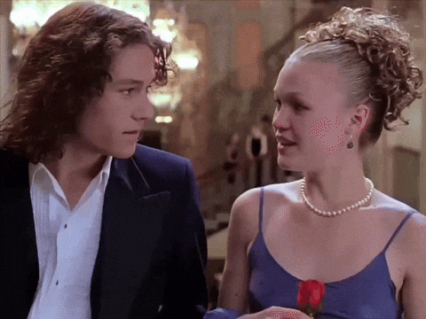 An animated GIF from 10 Things I Hate About You showing Patrick Verona (Heath Ledger) gazing affectionately at Kat Stratford (Julia Stiles) while she smiles back holding a red rose at prom—the ultimate late-90s Shakespearean teen romance moment.