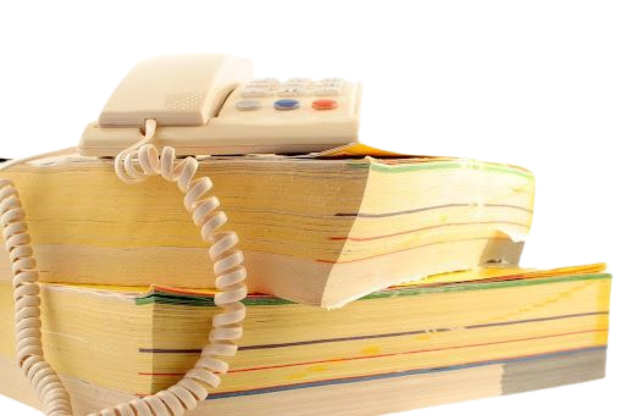 A landline corded phone resting atop a massive stack of worn, thick yellow pages telephone directories.