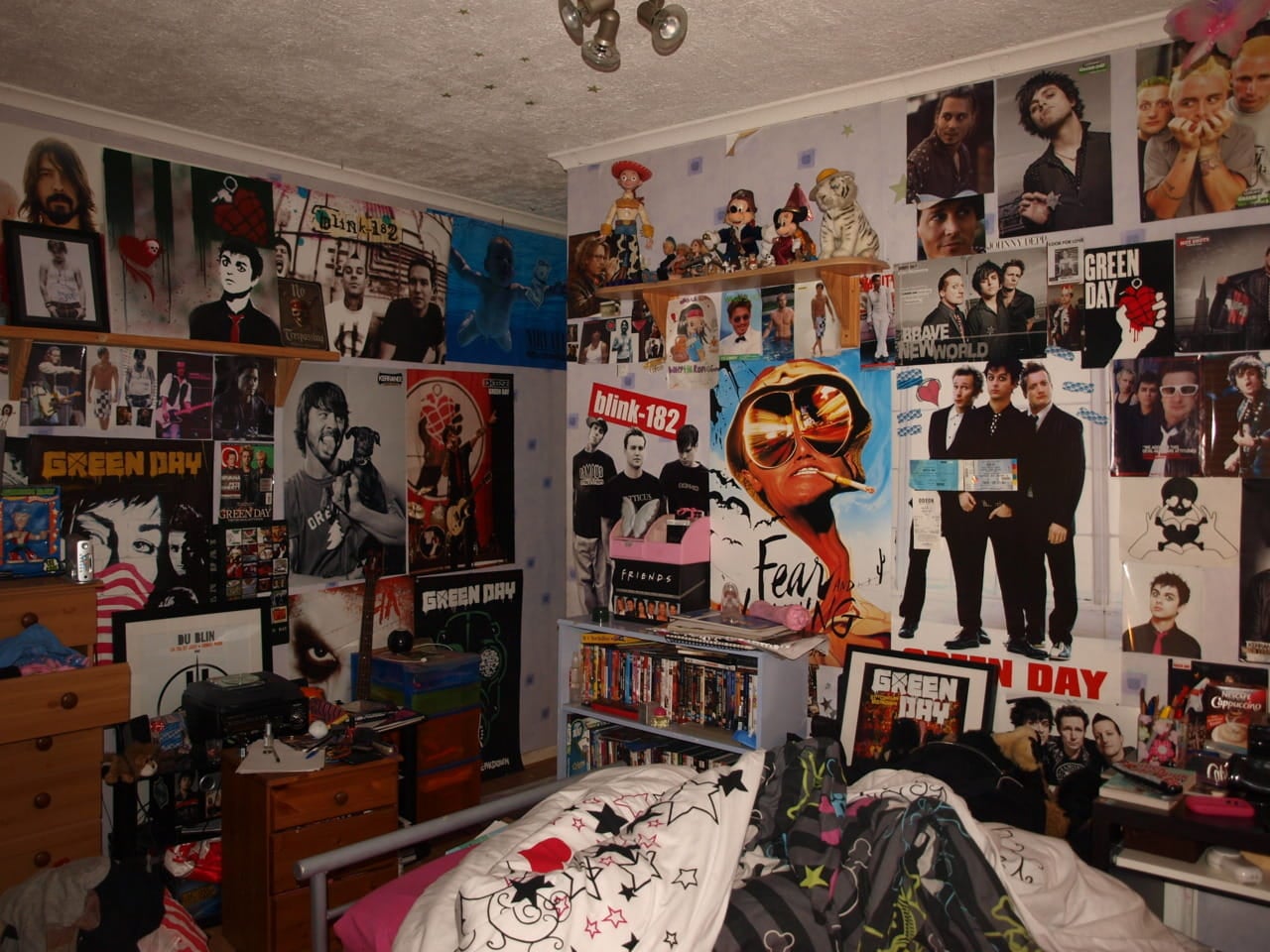 A teenager's bedroom wall completely plastered in pop-punk and alternative rock posters, featuring Green Day, Blink-182, Nirvana, and Fear and Loathing in Las Vegas.