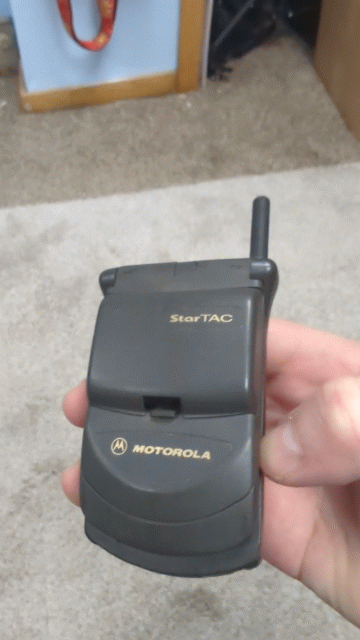 hand opening and closing the ultra-compact dark grey Motorola StarTAC, the defining Y2K status-symbol clamshell cellular phone.
