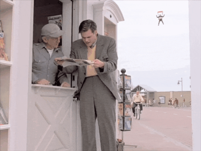 An animated GIF from The Truman Show showing Truman Burbank frantically reading a newspaper at a newsstand, completely unaware of a parachutist glitching into the artificial sky backdrop behind him.