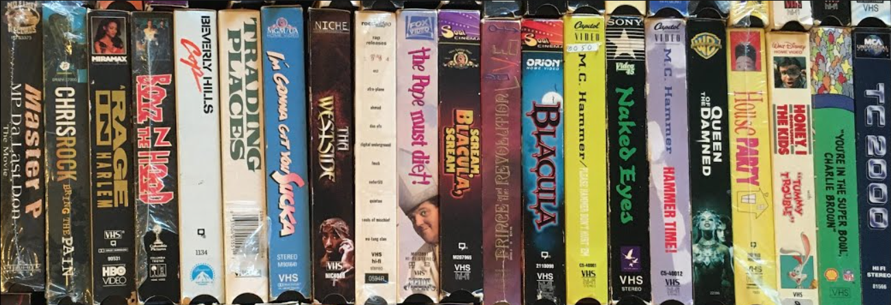 A vertical stack of 90s hip-hop, comedy, and drama VHS tape spines including House Party, M.C. Hammer concert tapes, Boyz n the Hood, Chris Rock's Bring the Pain, and Master P's MP Da Last Don.