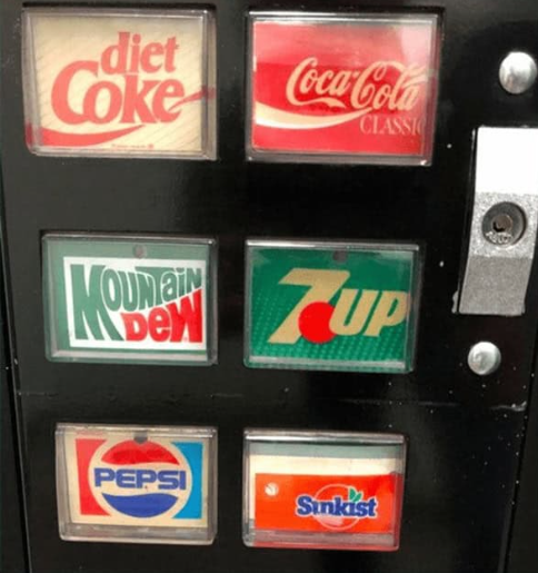 A classic black 90s vending machine selection panel featuring backlit retro logo buttons for Diet Coke, Coca-Cola Classic, Mountain Dew, 7UP, Pepsi, and Sunkist.