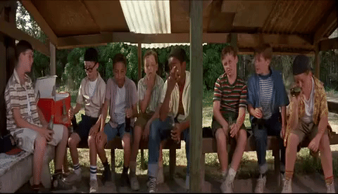An animated GIF from The Sandlot showing the neighborhood kids sitting together under their wooden dugout shelter, trying Big Chief chewing tobacco before getting sick on the carnival ride.