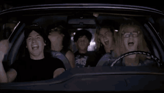 An animated GIF from Wayne's World showing Wayne Campbell (Mike Myers), Garth Algar (Dana Carvey), and their crew driving in the AMC Pacer 'Mirthmobile' while headbanging wildly to Queen's 'Bohemian Rhapsody.'