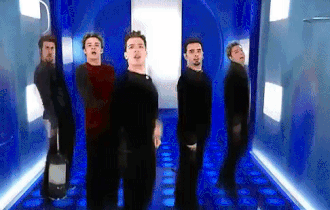 An animated GIF from 'NSYNC's "Bye Bye Bye" music video, showing Justin Timberlake, JC Chasez, and the group executing their iconic puppet-string arm choreo in a blue tunnel.