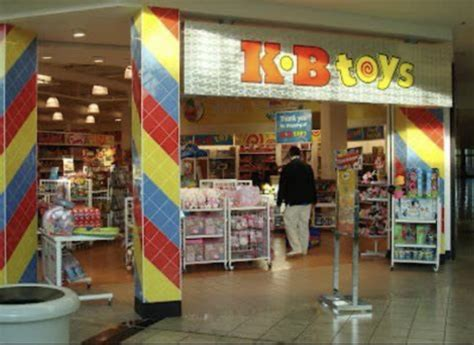 An entrance view of a 90s KB Toys mall location, flanked by colorful primary-striped entry pillars and floor-to-ceiling shelves stacked with action figures and board games.