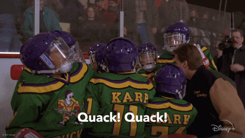 An animated GIF from The Mighty Ducks showing Coach Gordon Bombay (Emilio Estevez) huddled with his youth hockey team on the ice as they raise their heads and chant 'Quack! Quack!' in unison.