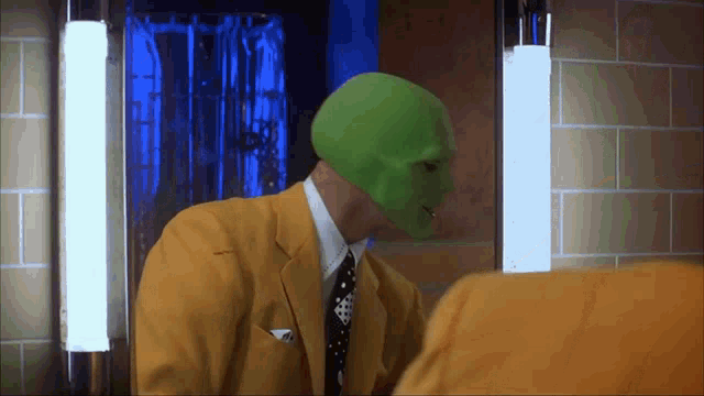 An animated GIF from The Mask featuring Stanley Ipkiss (Jim Carrey) transformed into the green-faced trickster, slicking back his hair in front of a mirror while wearing his iconic zoot suit.