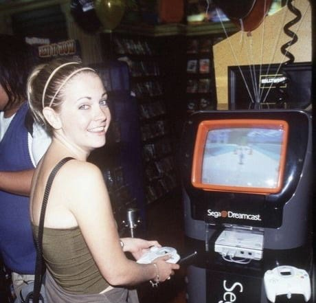 Sega Dreamcast Kiosk at Hollywood Video Teenager playing a 1999 Sega Dreamcast interactive display unit inside a Hollywood Video rental store, holding the oversized white controller next to a glowing CRT demo station.