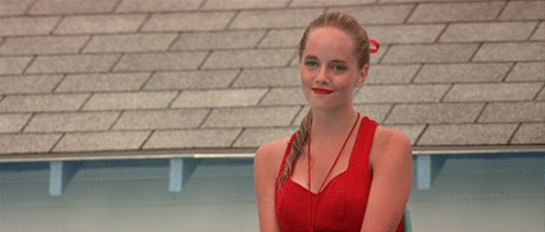 An animated GIF from The Sandlot showing lifeguard Wendy Peffercorn (Marley Shelton) sitting poolside in her iconic red swimsuit, smiling and giving a playful wave.