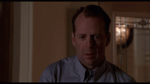 An animated GIF from The Sixth Sense showing child psychologist Dr. Malcolm Crowe (Bruce Willis) looking visibly unsettled and anxious as he slowly turns his head inside a dimly lit room.