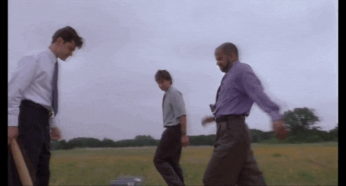 An animated GIF from Office Space showing Peter, Samir, and Michael Bolton surrounding a malfunctioning office printer in an open field, taking turns violently stomping and smashing it with a baseball bat.