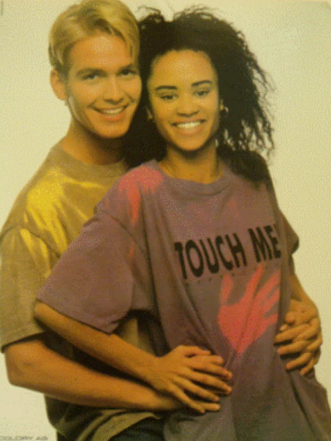 A 90s couple smiling together, with the woman wearing a purple heat-sensitive Global Hypercolor t-shirt that turns bright pink where her hands touch it—the ultimate interactive 90s fashion statement.