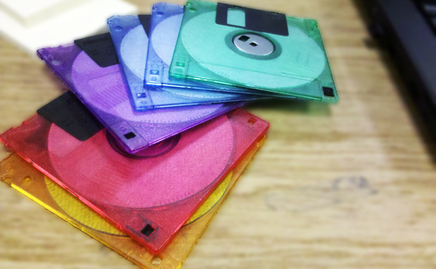 fanned-out stack of 1990s translucent neon 3.5-inch floppy disks in jewel-toned purple, teal, blue, red, and yellow plastic.