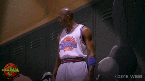 An animated GIF from Space Jam showing Michael Jordan sitting in the Tune Squad locker room wearing his white jersey, looking down while Bugs Bunny leans in to give him a motivational prep talk.