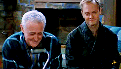 Animated GIF from the Frasier episode 'Momma Mia' showing Frasier, Martin holding his cane, and Niles sitting together on the couch, emotionally watching a home video of their late mother/wife Hester blowing a kiss from the TV screen.