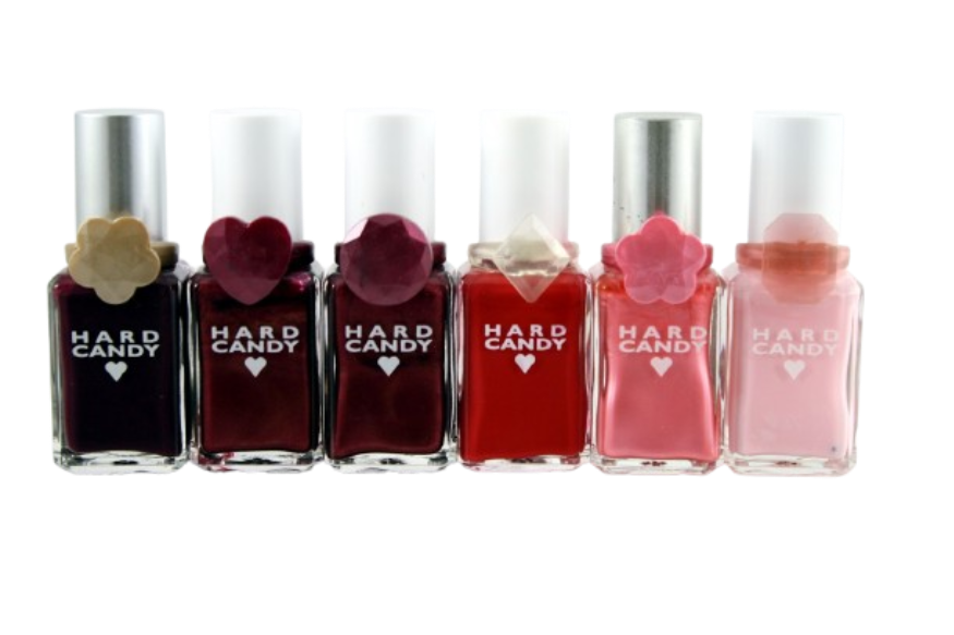 A lineup of six 90s Hard Candy nail polish bottles in various shades of red and pink, each adorned with its collectible plastic flower or heart ring around the neck.
