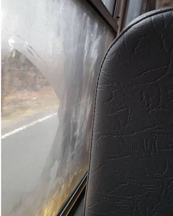 cracked dark-grey vinyl school bus seat next to a fogged-up window where generations of kids drew hearts and smiley faces during cold morning commutes.