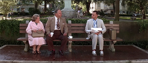 An animated GIF from Forrest Gump showing Forrest (Tom Hanks) sitting on a park bench offering a chocolate from his box to the woman sitting next to him.