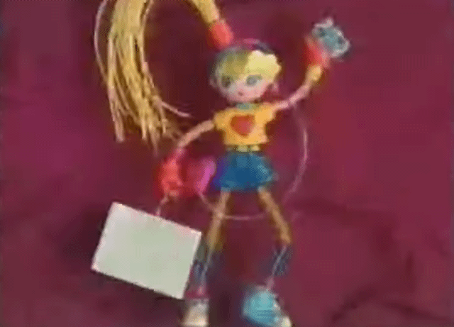 An animated GIF from a retro TV commercial showing a flexible Betty Spaghetty doll with bendy yellow rubber hair, a clip-on denim skirt, and removable hands holding a shopping bag.