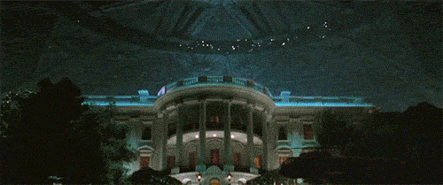 An animated GIF from Independence Day showing a massive alien mothership firing its brilliant blue primary laser beam directly down onto the White House, detonating the entire building in a iconic 90s special-effects explosion.