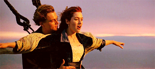 An animated GIF from Titanic showing Jack Dawson (Leonardo DiCaprio) holding Rose DeWitt Bukater (Kate Winslet) at the bow of the ship, arms outstretched over the ocean as the sun sets.