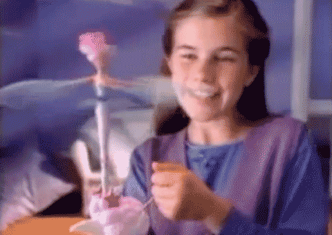 An animated GIF from a 90s Sky Dancers commercial showing a young girl pulling the launcher cord to spin a pink fairy doll high into the air.