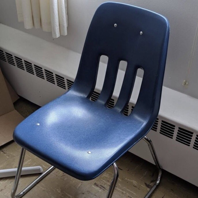 A classic navy-blue molded plastic school chair with metal legs and three vertical back vents, sitting next to a classroom radiator.