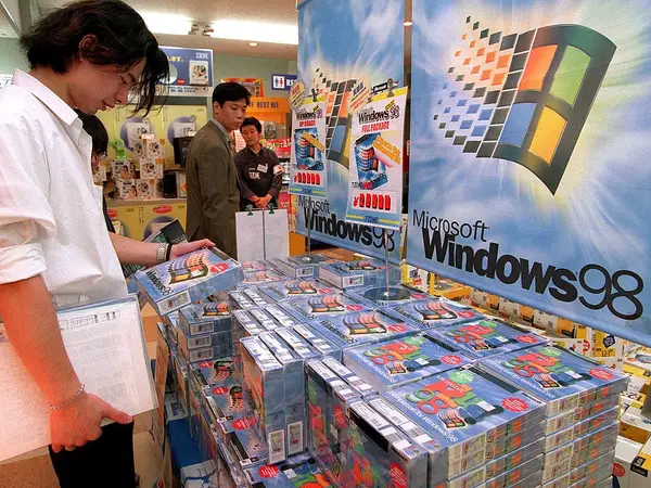 A retail store display filled with stacks of boxed Microsoft Windows 98 software packages and promotional banners during the operating system's launch.